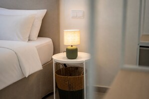 A neatly made bed with white linens, a round table with a green lamp, and a wicker basket underneath. - Stylish Apartament in the Heart of Olhao, Algarve (Olhão)