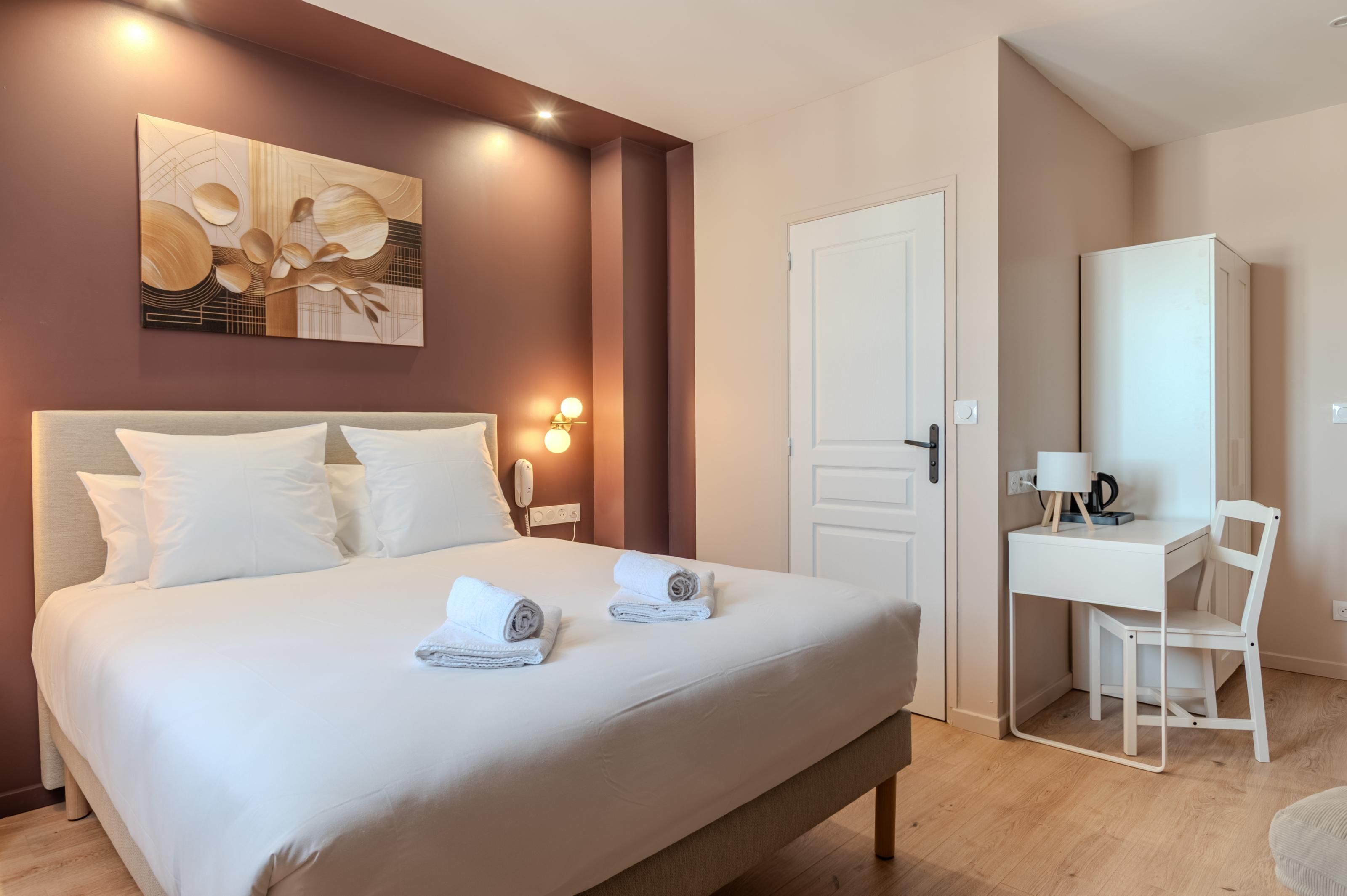 Una camera d'albergo con un letto, una scrivania, una sedia, un armadio e un quadro appeso al muro.