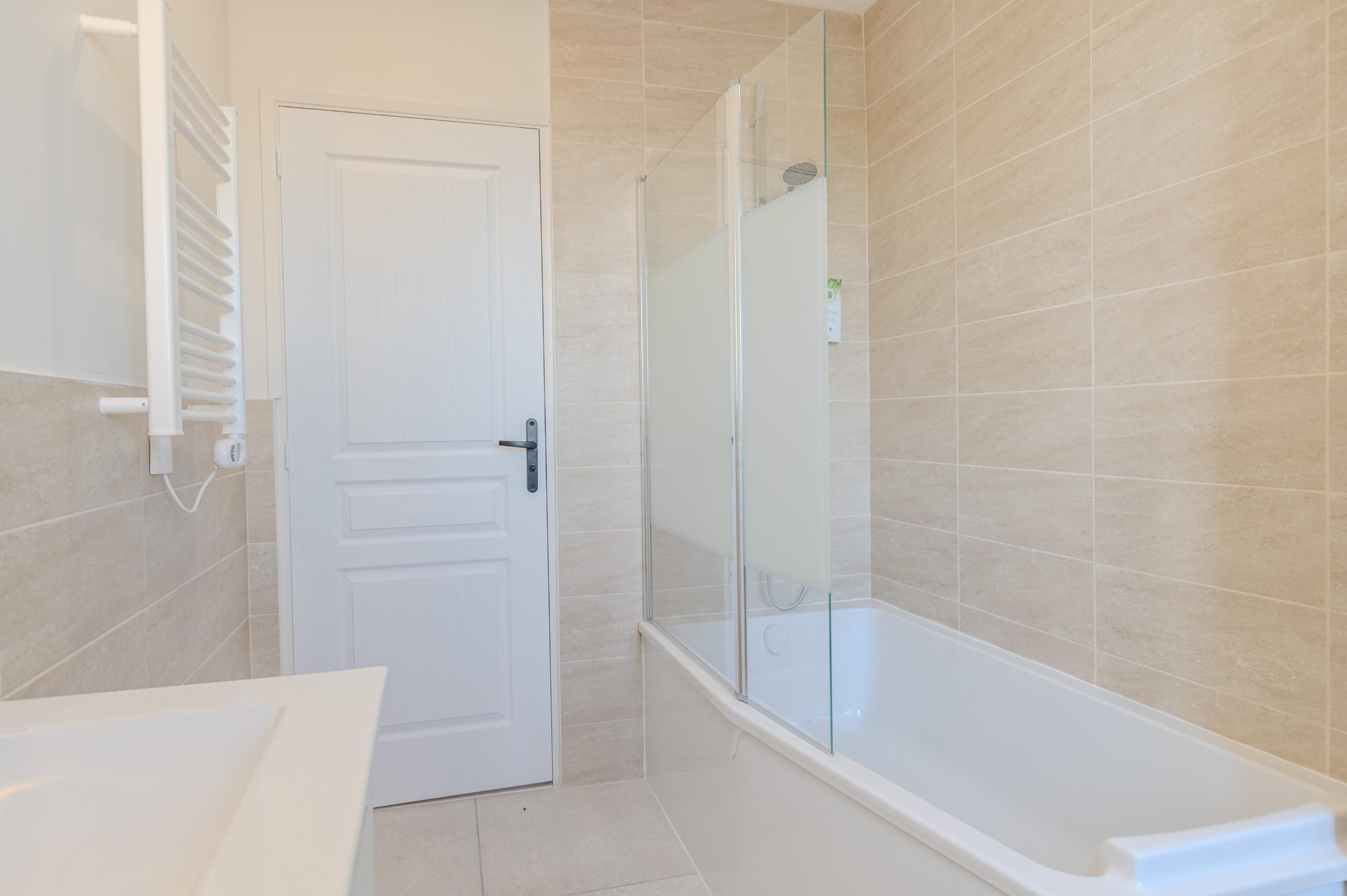 A bathroom with a white door, a glass shower enclosure, and a white bathtub.