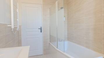 A bathroom with a white door, a glass shower enclosure, and a white bathtub.