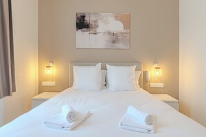 A hotel room with a large bed, two bedside lamps, a painting on the wall, and two rolled towels on the bed. - Grand Hôtel de la Gare (Abbeville)