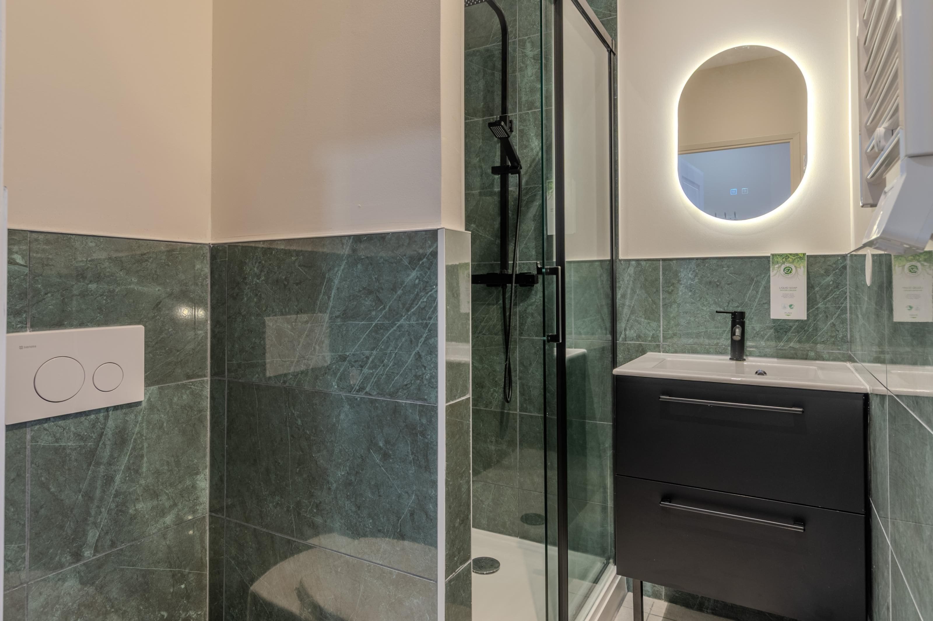 A modern bathroom with a glass shower enclosure, a vanity with a black sink, and a wall-mounted mirror.