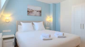 A bedroom with a bed, two bedside tables, a nightstand, a wall-mounted telephone, and a door.