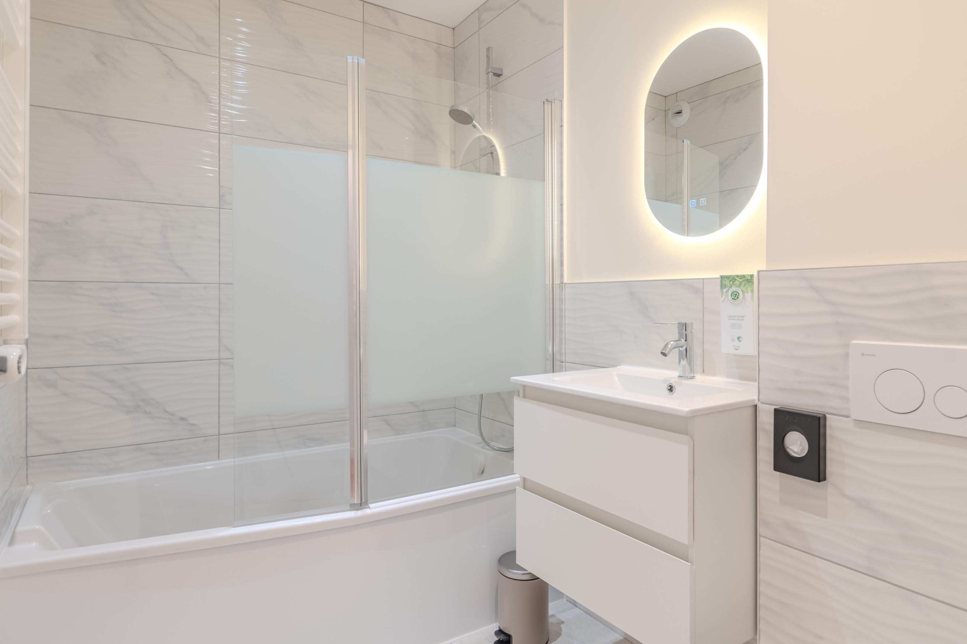 A modern bathroom with a glass-enclosed shower, a white sink, and a mirror with a circular frame.