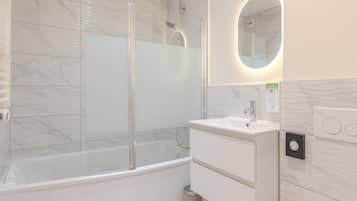 A modern bathroom with a glass-enclosed shower, a white sink, and a mirror with a circular frame.