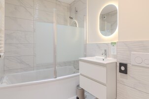 A modern bathroom with a glass-enclosed shower, a white sink, and a mirror with a circular frame.