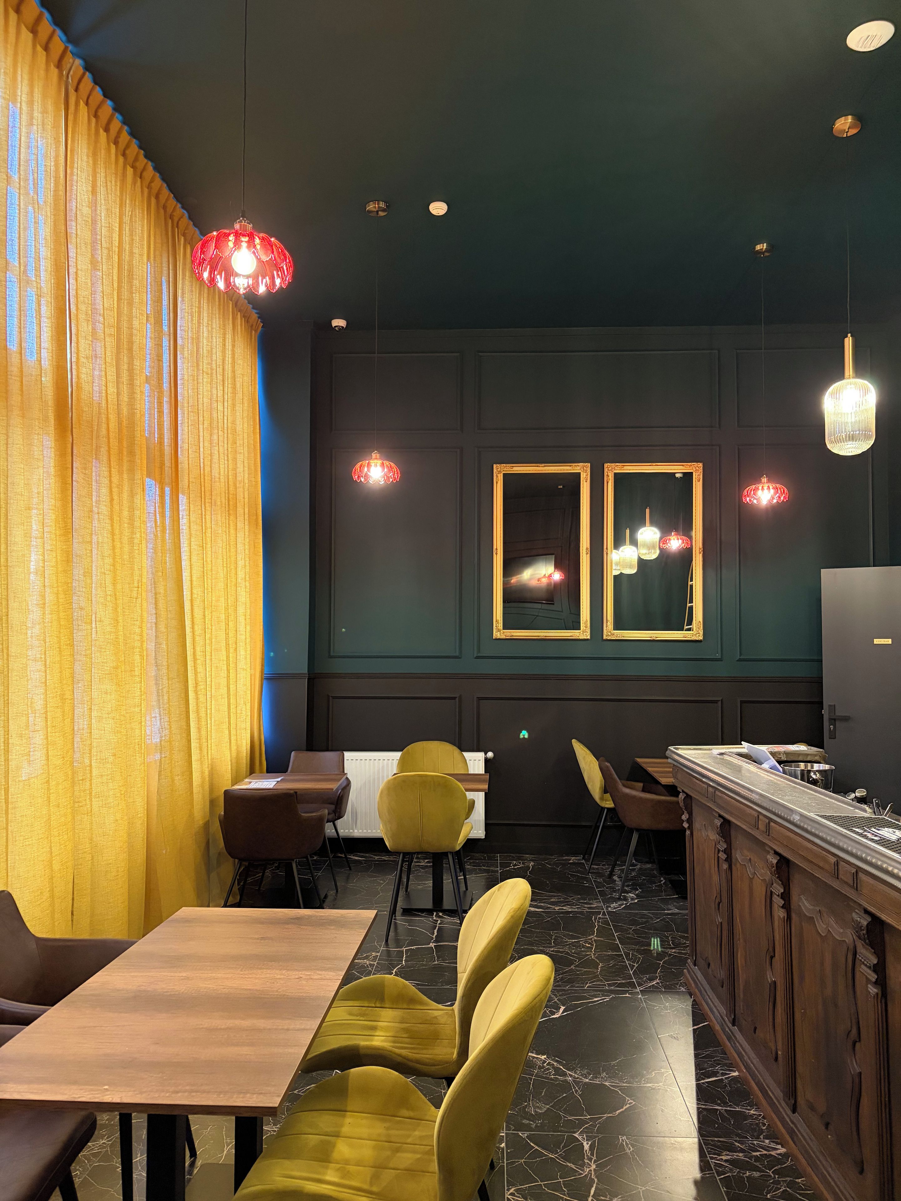 Een restaurantinterieur met een bar, gele stoelen en hanglampen.