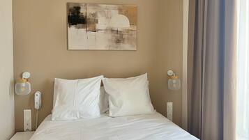 A hotel room with a bed, a painting on the wall, a telephone, and a lamp.