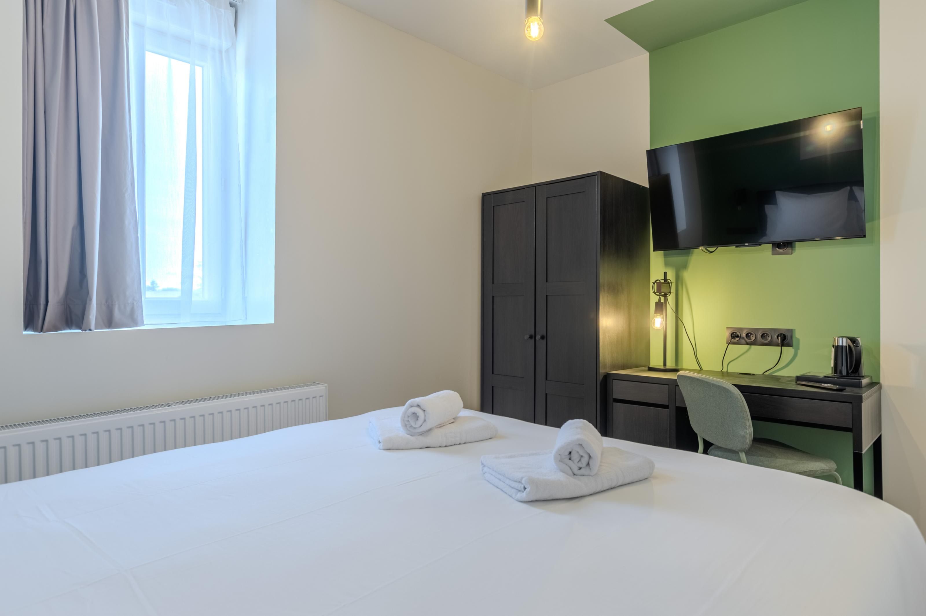 Ein Hotelzimmer mit einem Bett, einem Schreibtisch, einem Fernseher und einem Kleiderschrank.