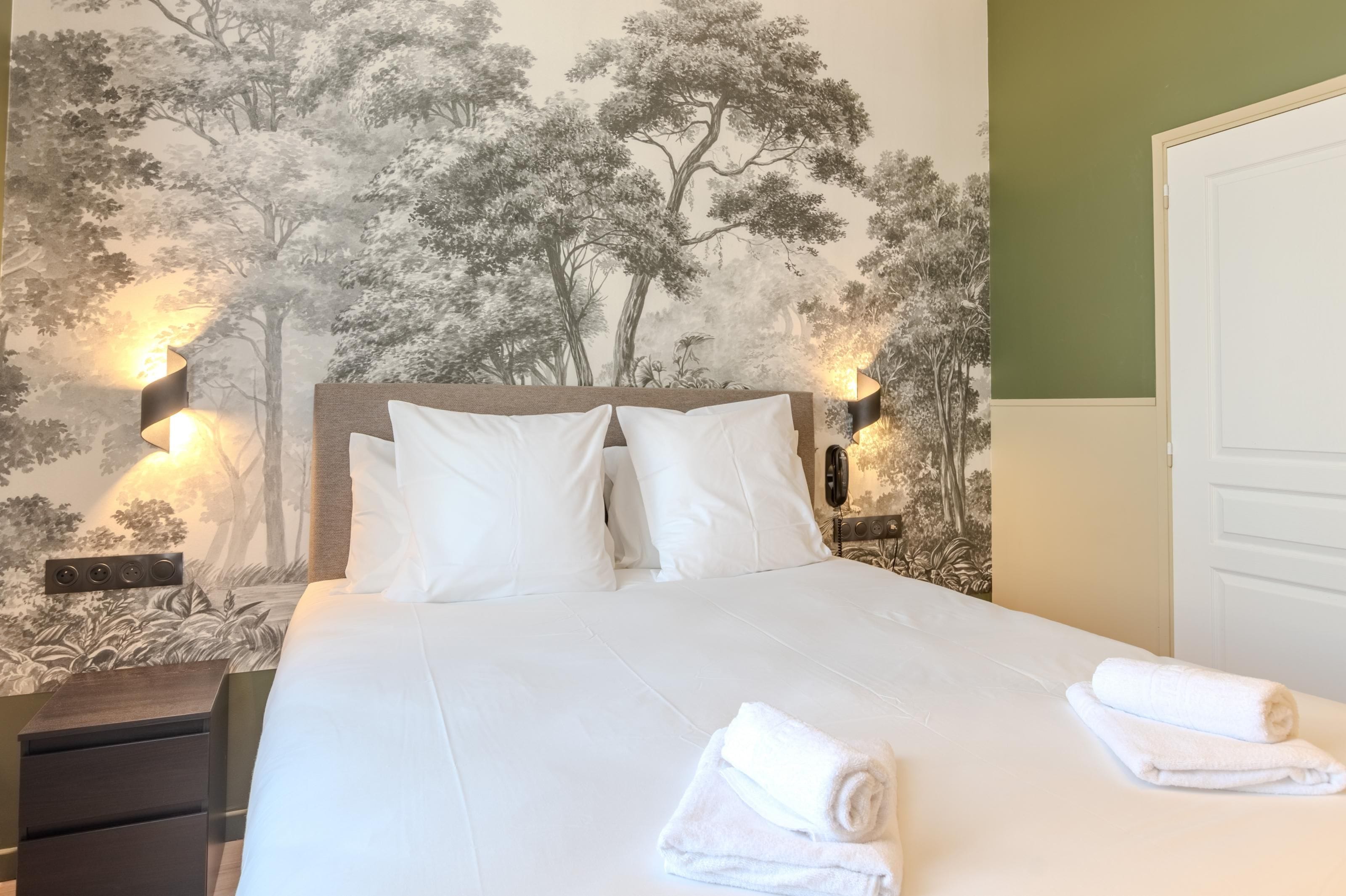 A hotel room with a bed, two bedside lamps, a nightstand, and a wall mural.