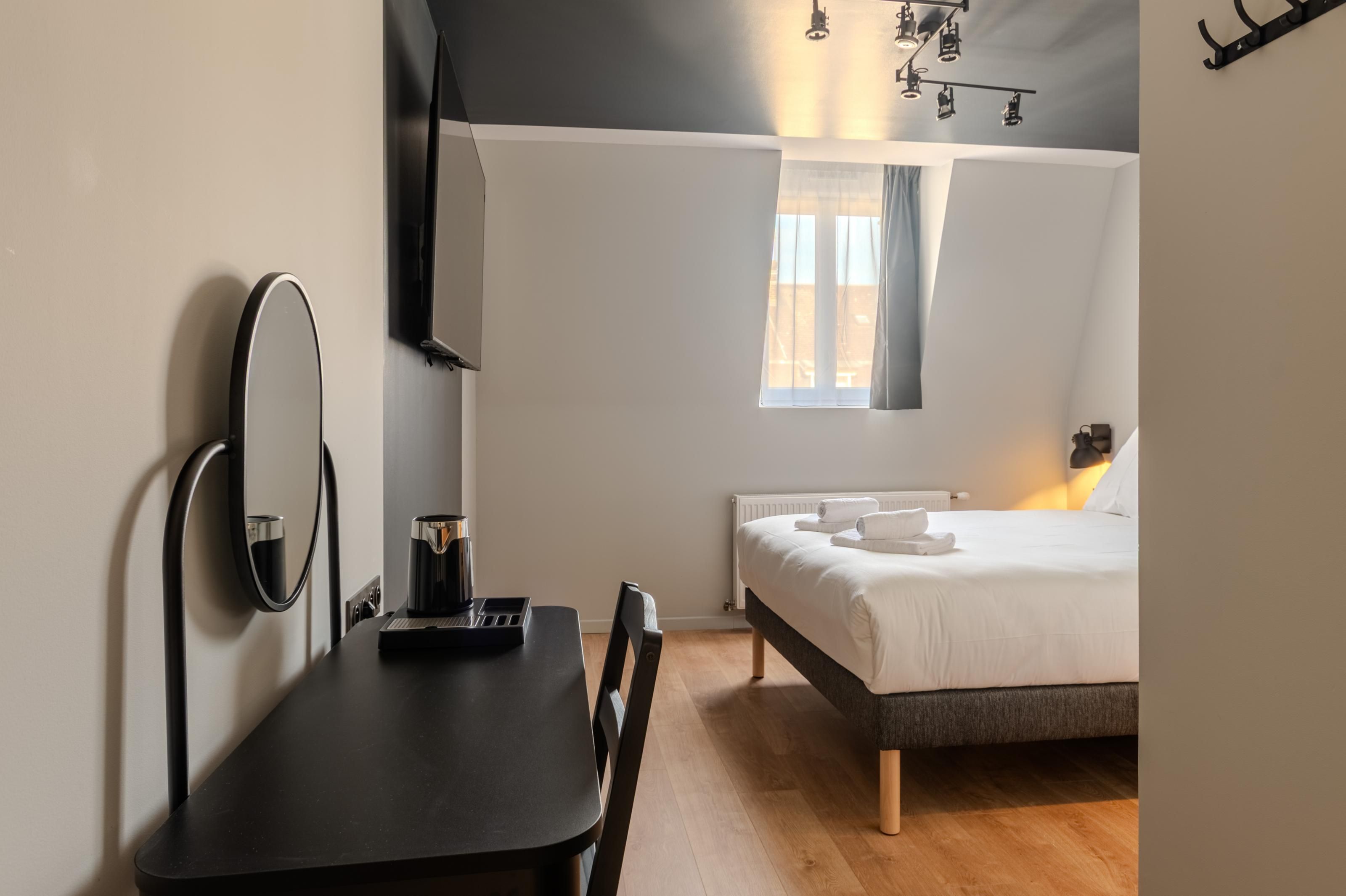 Una camera da letto con un letto, un comodino, uno specchio, una finestra con tende e una lampada a sospensione.
