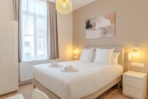 A hotel room with a bed, bedside lamps, a painting on the wall, and a window with curtains.