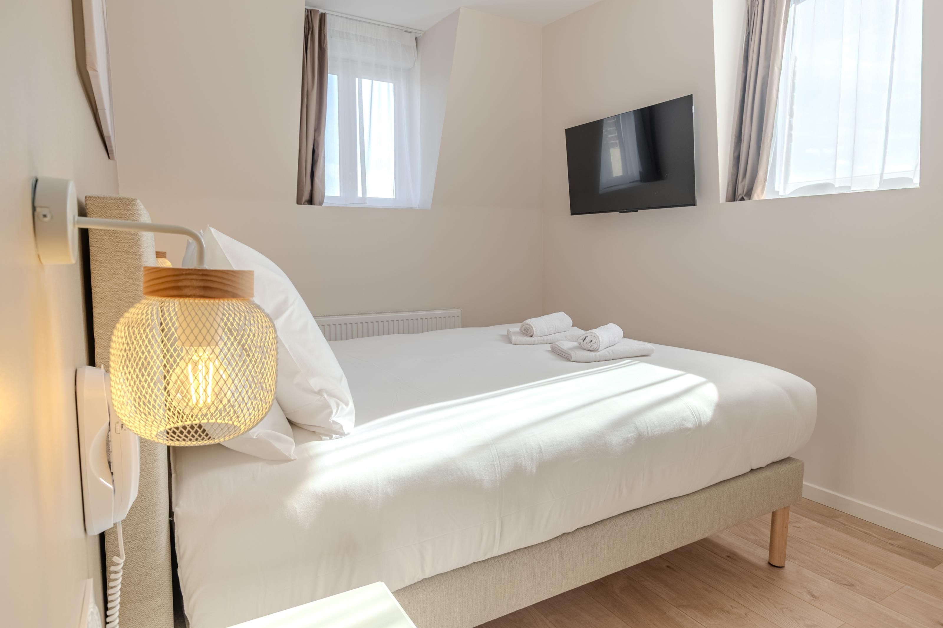 Un dormitorio con cama, televisión montada en la pared y lámpara.