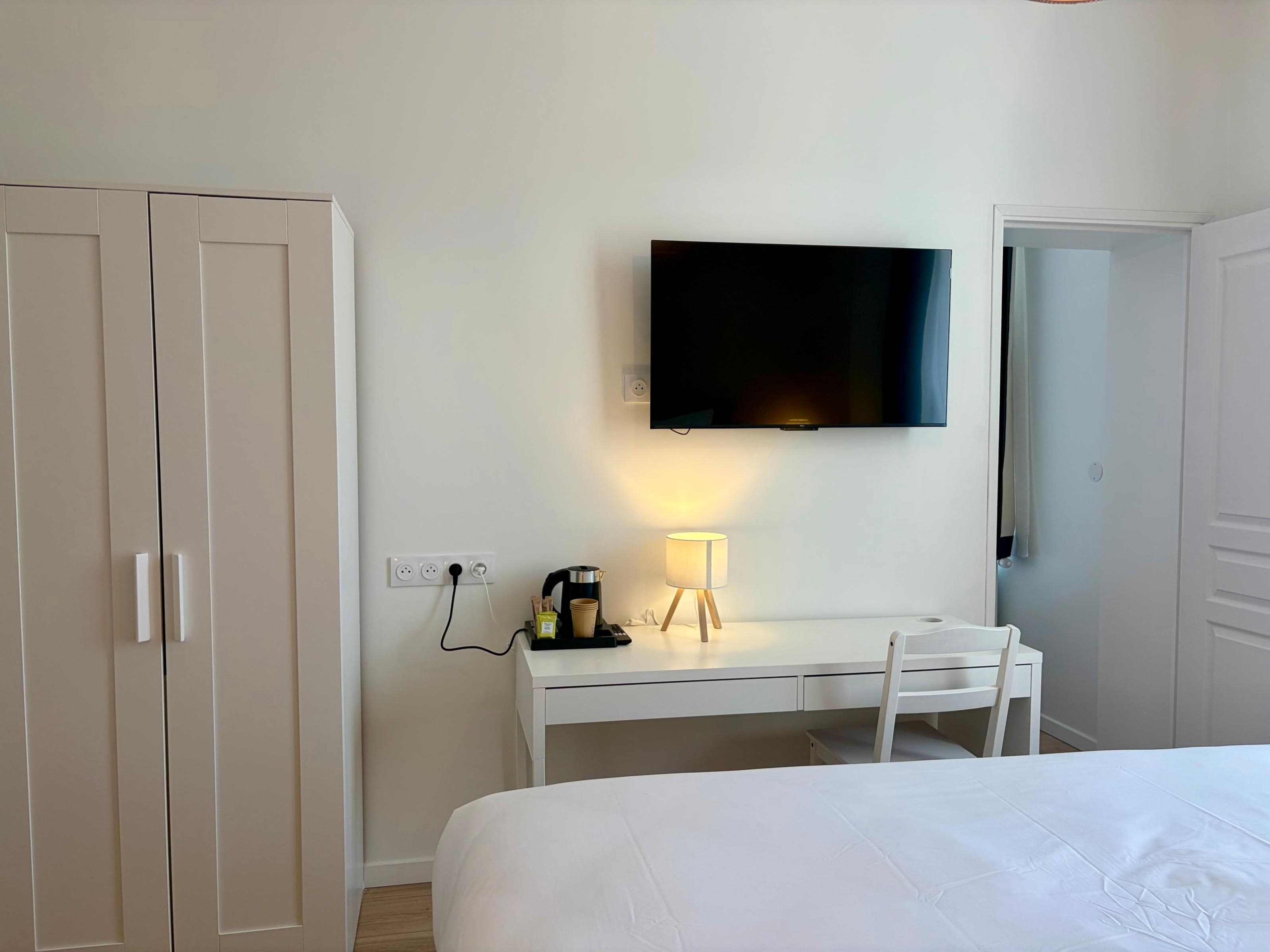 A hotel room with a bed, a desk with a lamp, a television, and a wardrobe.