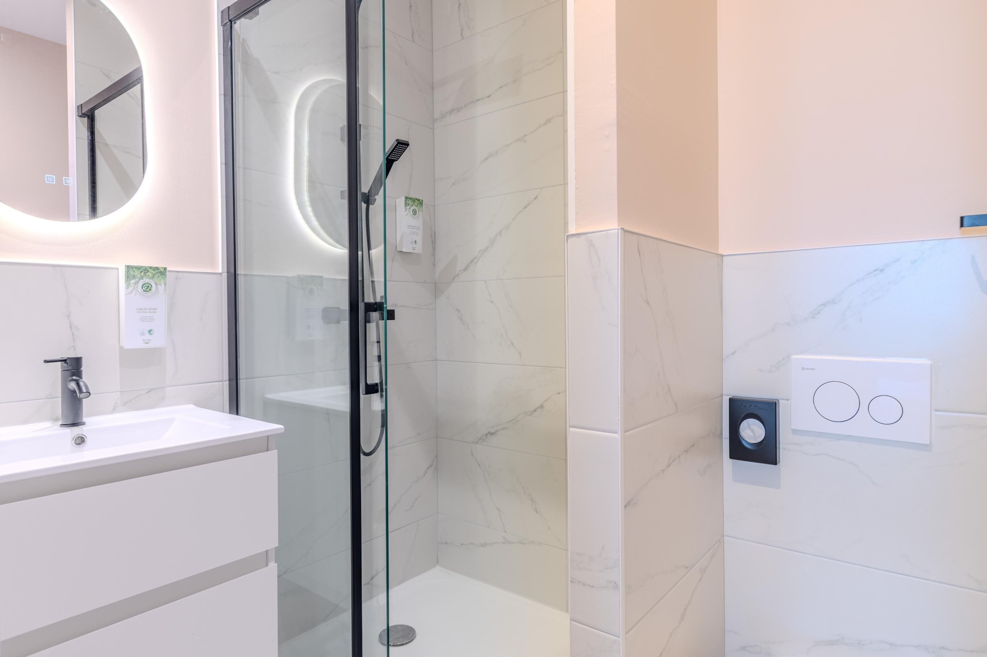 A modern bathroom with a glass-enclosed shower, a white sink, and a marble-tiled wall.