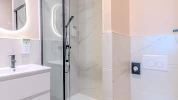A modern bathroom with a glass-enclosed shower, a white sink, and a marble-tiled wall.