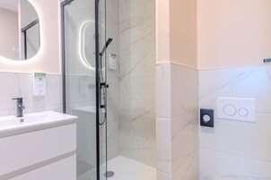 Un baño moderno con ducha envuelta en vidrio, un lavamanos blanco y una pared con azulejos de mármol.