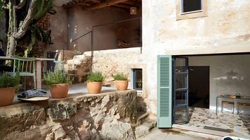 Un mur de pierre agrémenté de plantes en pot, un escalier et une porte vitrée donnant sur un espace intérieur doté d’un sol carrelé.