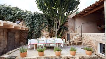 An outdoor dining area with a table set for four, surrounded by potted plants and a large cactus.