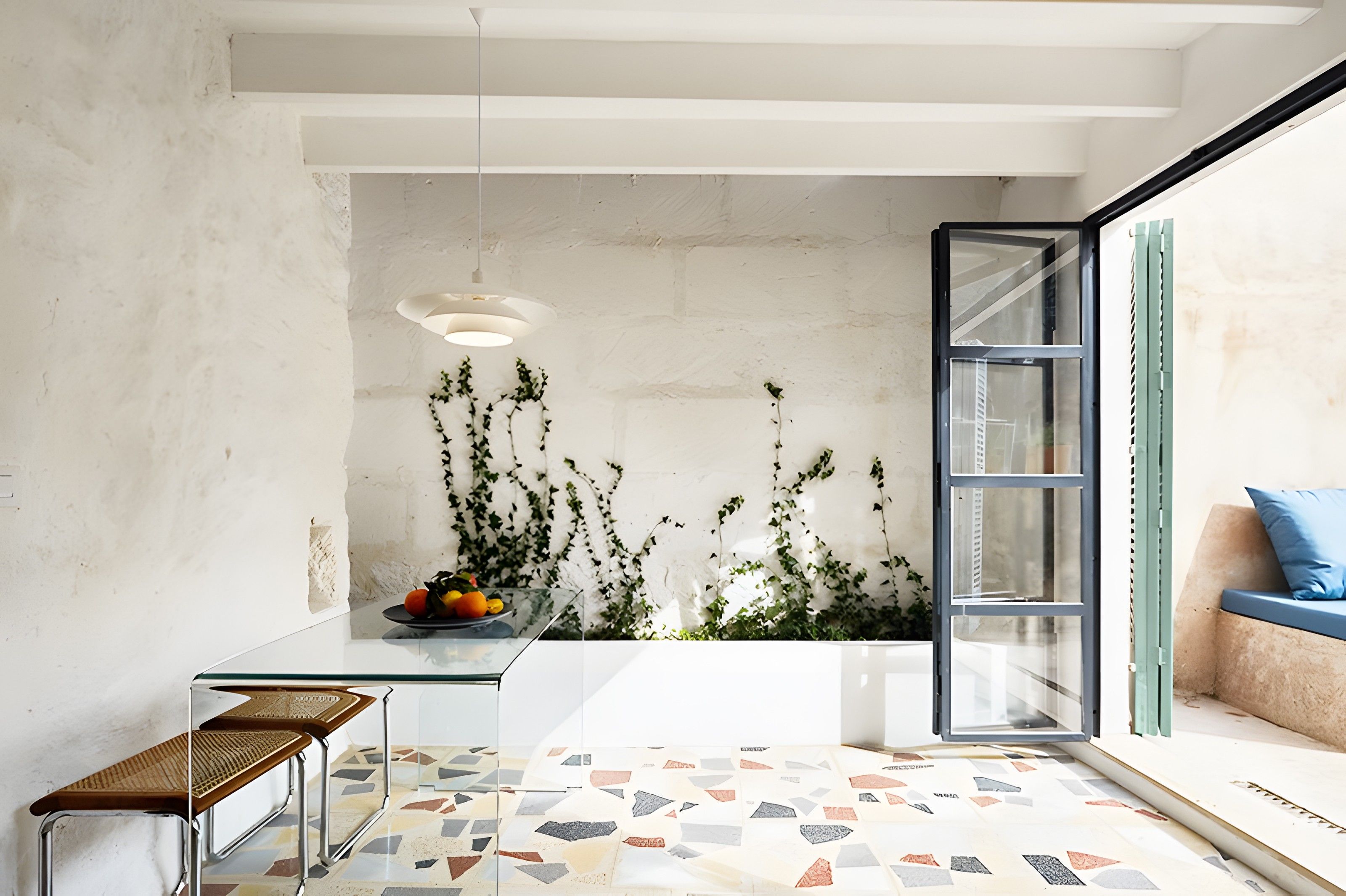 Un interior moderno con zona de comedor, un sofá con cojín, una lámpara colgante y vistas a través de un ventanal.