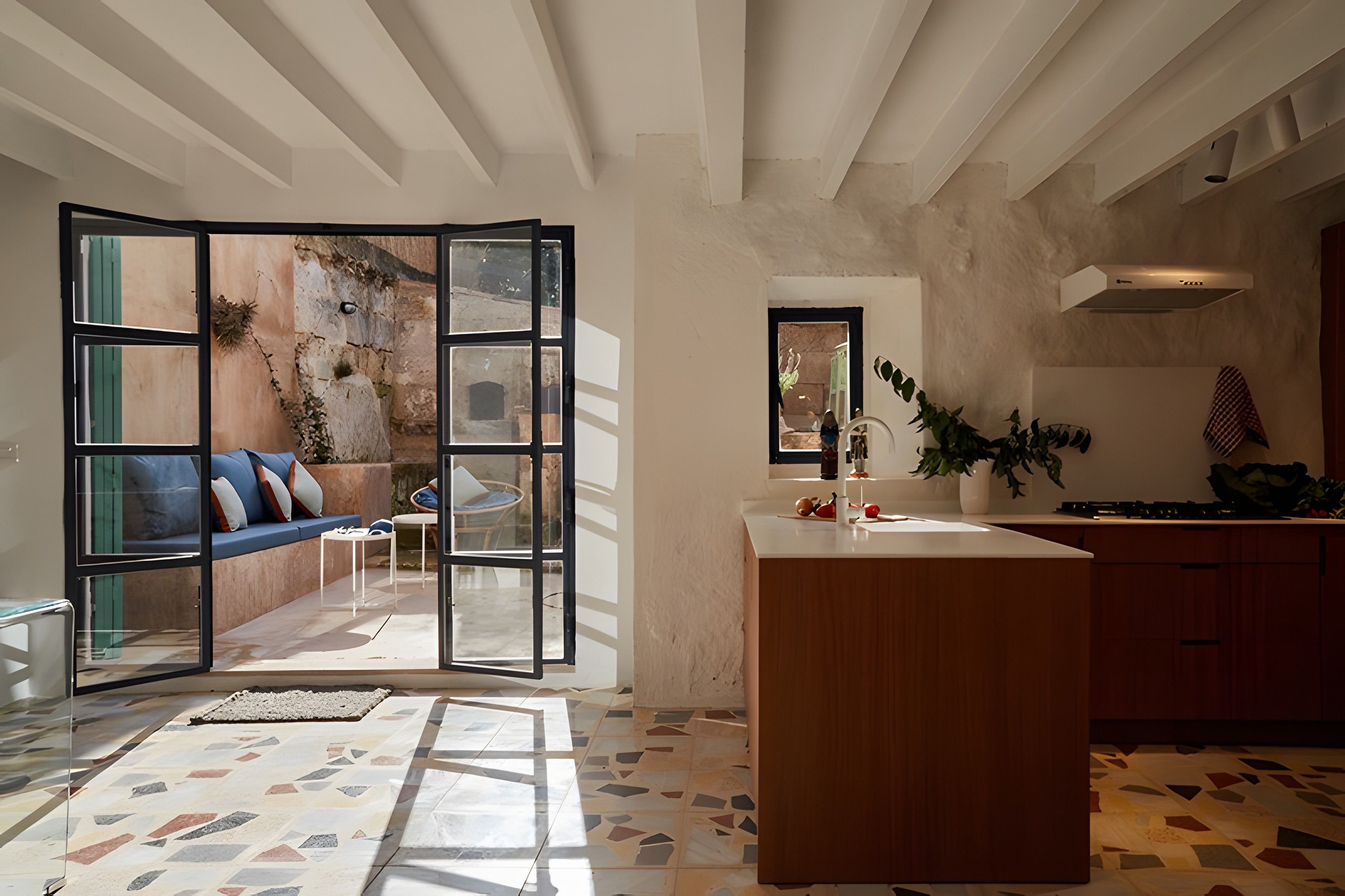 Cocina moderna con una isla central, comedor con sofá y sillas, y vistas a un espacio exterior a través de un panel de vidrio.