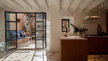 Cocina moderna con una isla central, comedor con sofá y sillas, y vistas a un espacio exterior a través de un panel de vidrio.
