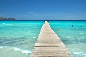 Une jetée en bois s’étendant dans une mer turquoise aux eaux limpides, avec une terre ferme visible au loin.