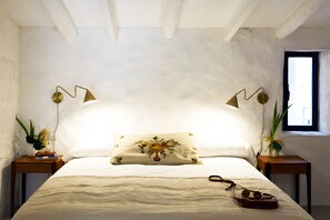 Un dormitorio con cama, dos mesitas de noche, una ventana y una lámpara de pared.