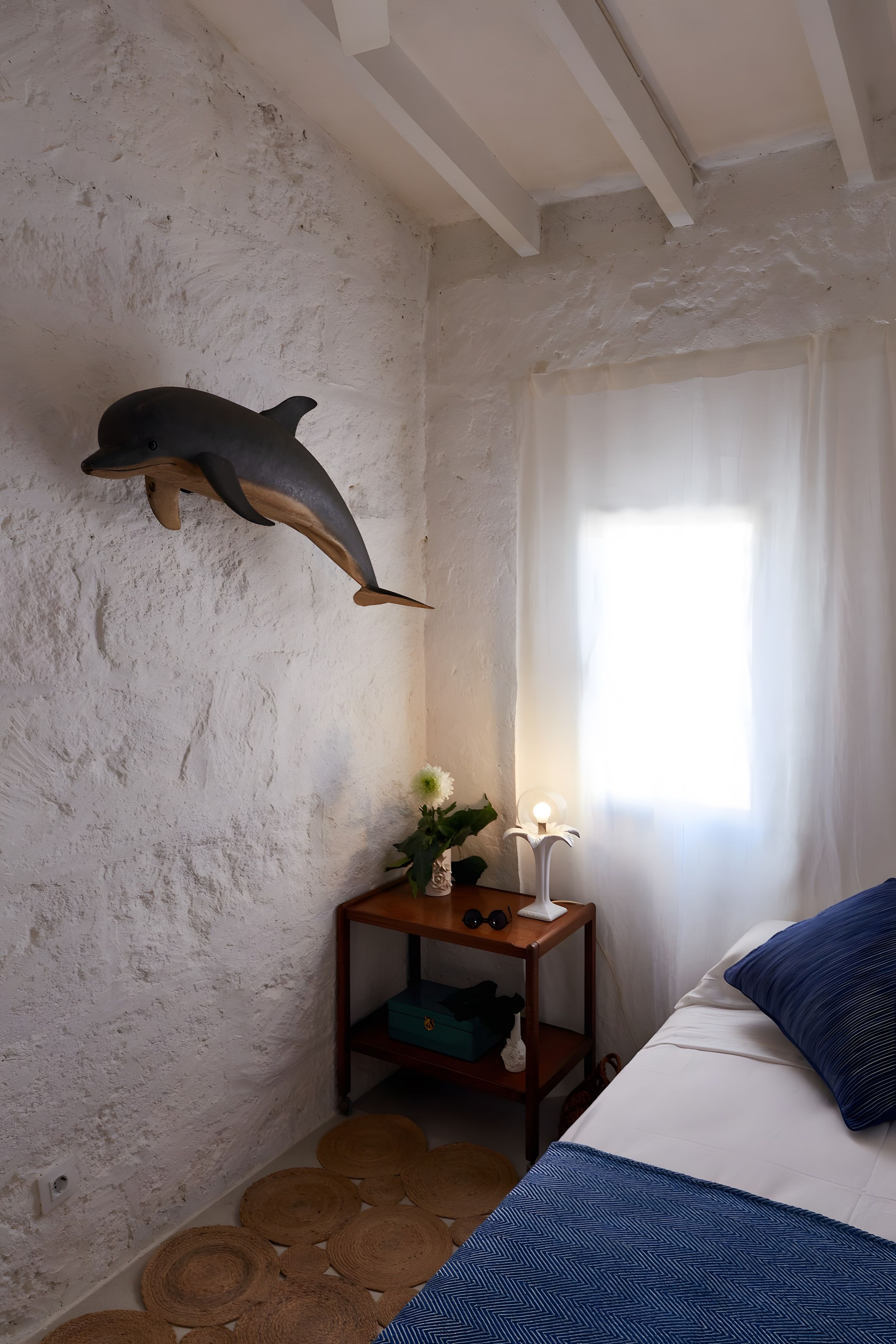 Een kamer met een decoratie van een dolfijn, een nachtkastje met een lamp en een bed met blauw beddengoed.