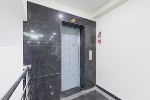 A modern elevator with a glass door, a fire extinguisher mounted on the wall, and a marble floor. - Capital O Regal suites (Bangalore)