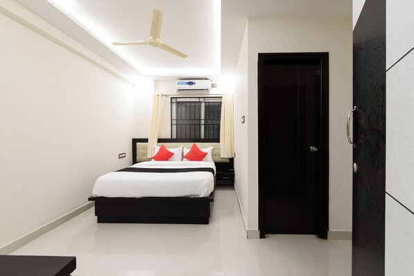 A hotel room with a bed, a ceiling fan, an air conditioning unit, a door, and a wardrobe.