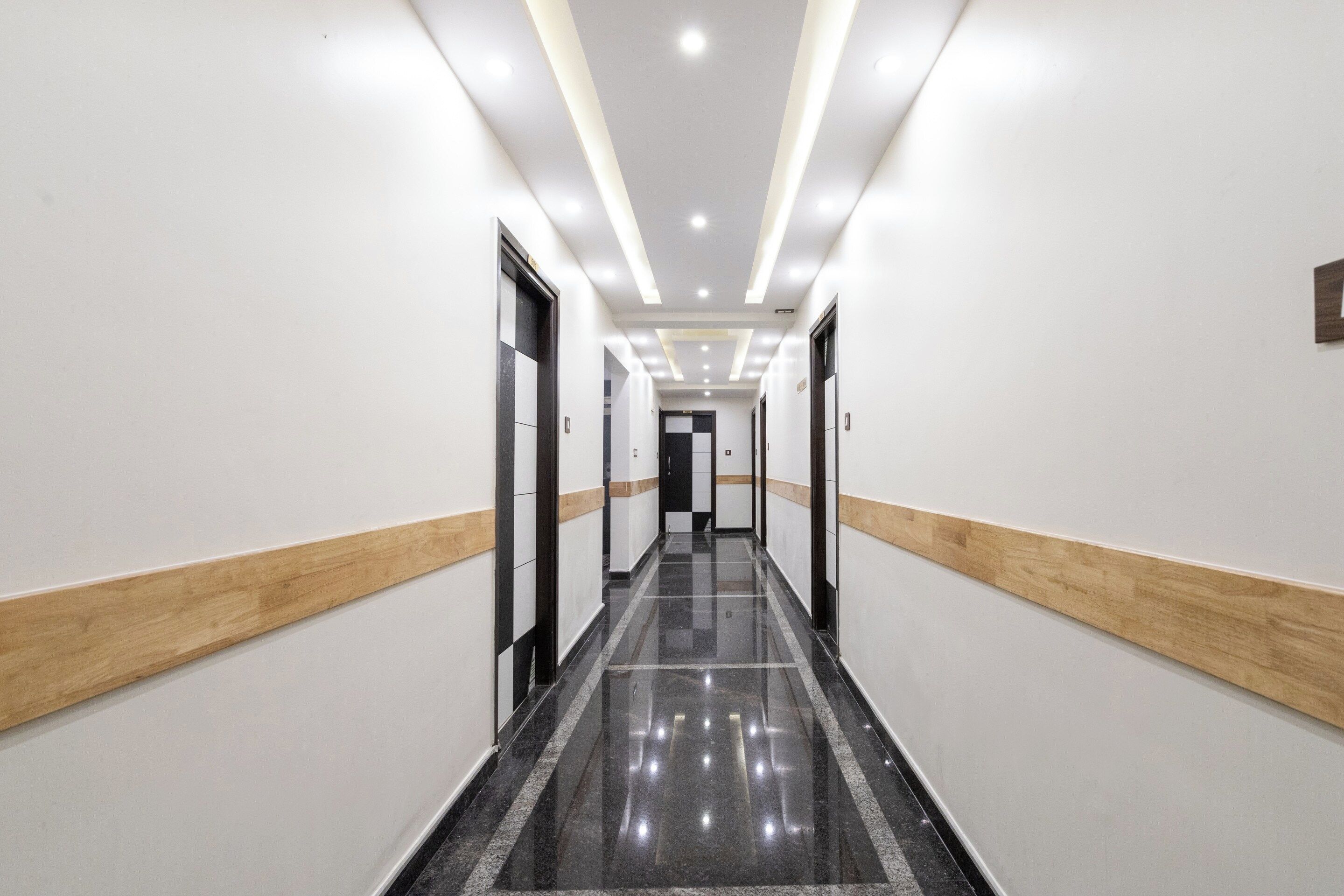 A long, narrow hallway with a polished black floor, white walls, and wooden paneling on the lower half.