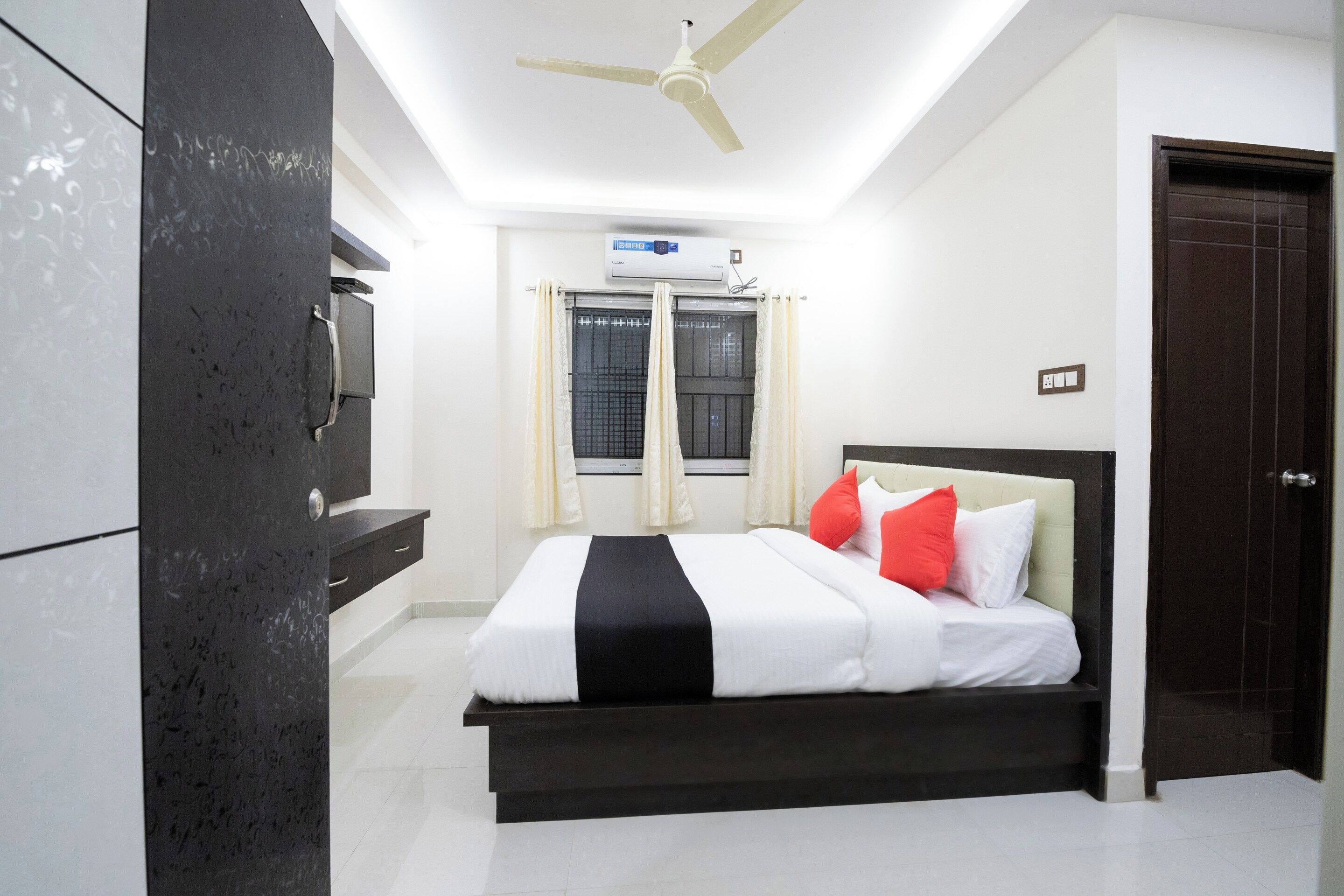 A bedroom with a bed, a ceiling fan, an air conditioning unit, and a window with curtains.