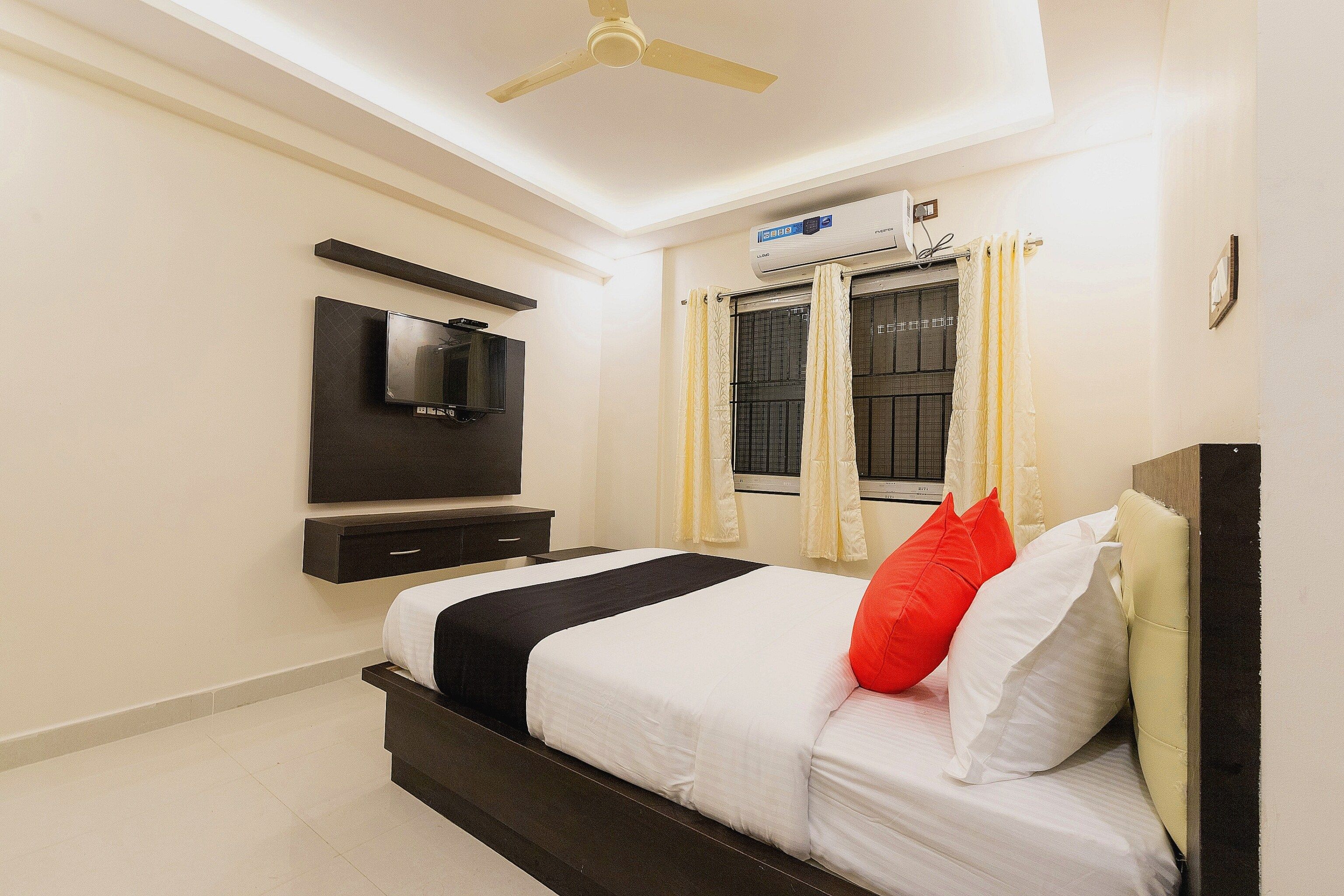 Una habitación de hotel con cama, televisión de pantalla plana montada en la pared, ventilador de techo y aire acondicionado.