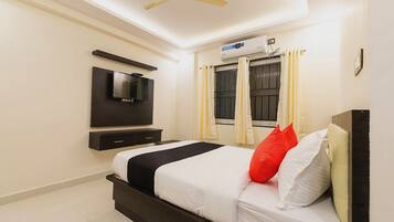 Una habitación de hotel con cama, televisión de pantalla plana montada en la pared, ventilador de techo y aire acondicionado.