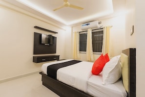 A hotel room with a bed, a flat-screen TV mounted on the wall, a ceiling fan, and an air conditioning unit.