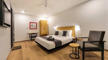 Una habitación de hotel con una cama, una silla, una mesita, un armario y un ventilador de techo.