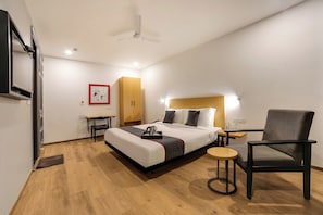 Una habitación de hotel con una cama, una silla, una mesita, un armario y un ventilador de techo.
