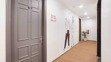 Un pasillo con una puerta gris marcada con el número 203, una pared con un letrero direccional para las habitaciones 201-202 y 203-207, y una planta en maceta cerca de una puerta.