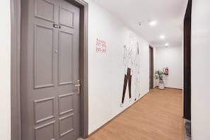 Un pasillo con una puerta gris marcada con el número 203, una pared con un letrero direccional para las habitaciones 201-202 y 203-207, y una planta en maceta cerca de una puerta.