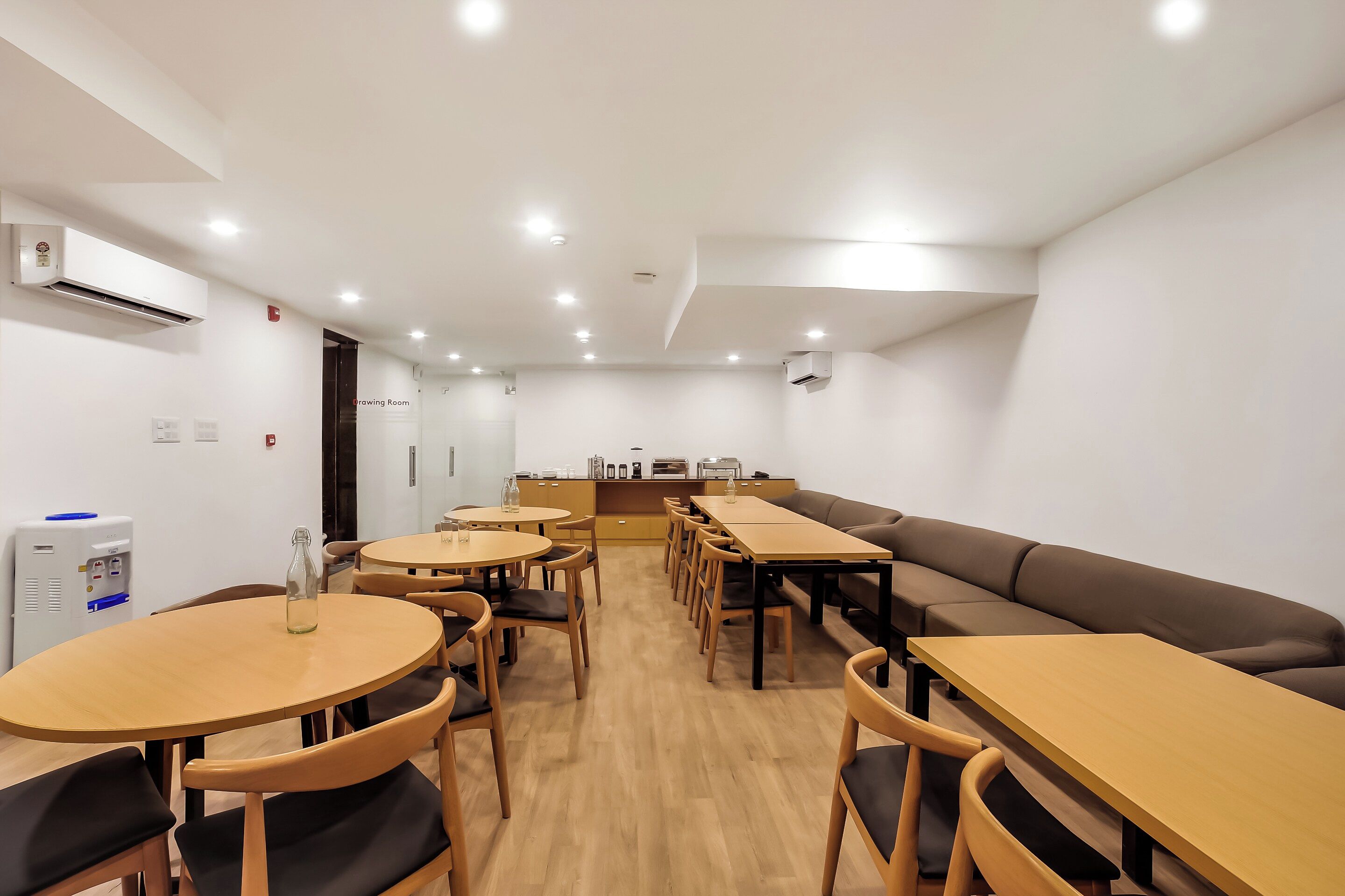 Un comedor moderno con mesas y sillas redondas, una larga mesa común y un sofá.