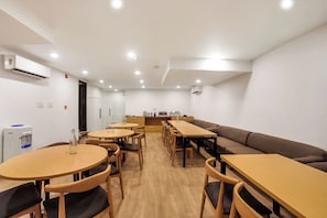 Un comedor moderno con mesas y sillas redondas, una larga mesa común y un sofá.