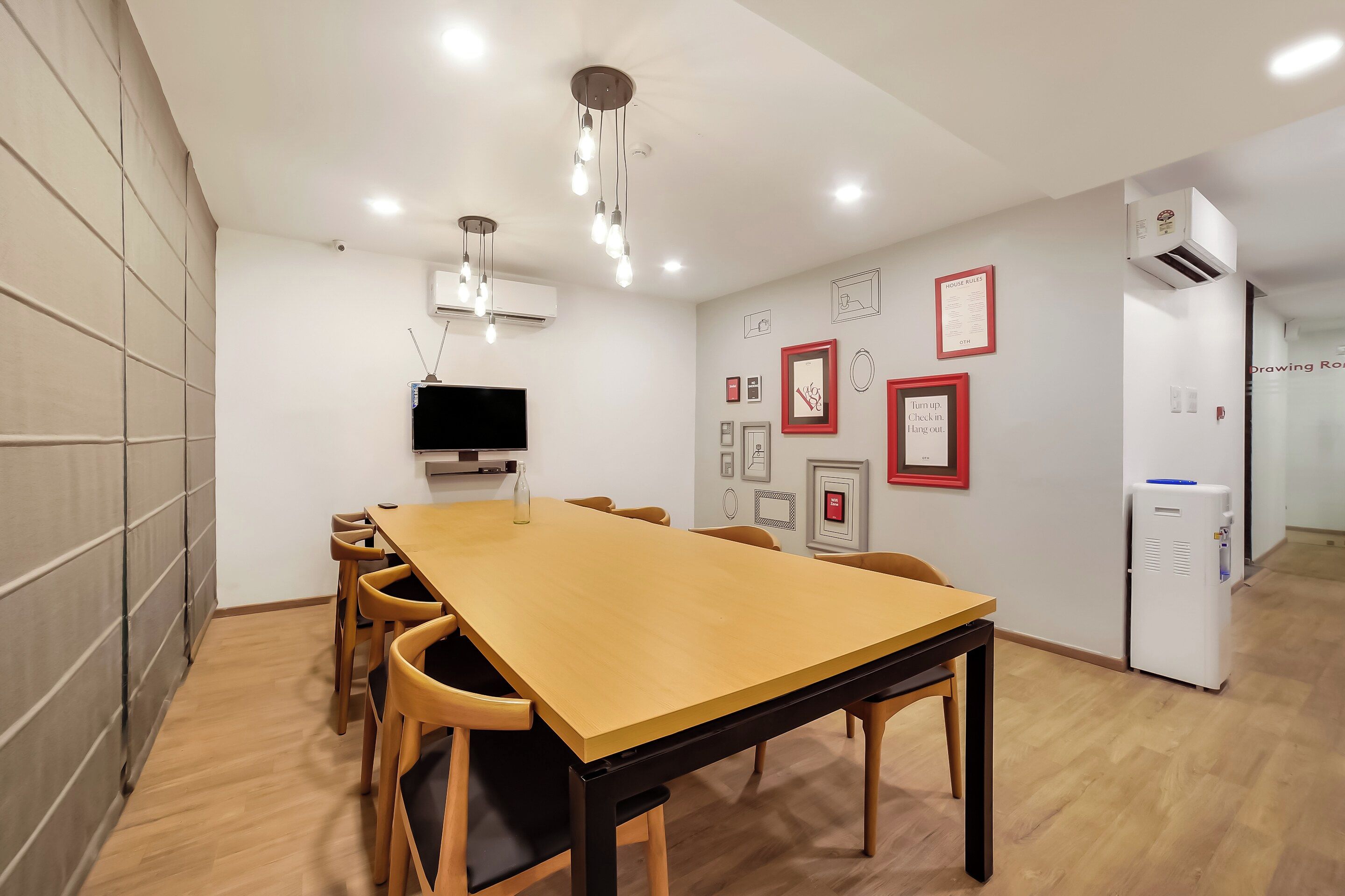 Un salón de conferencias con una larga mesa, sillas, un televisor de pantalla plana y aire acondicionado instalado en la pared.