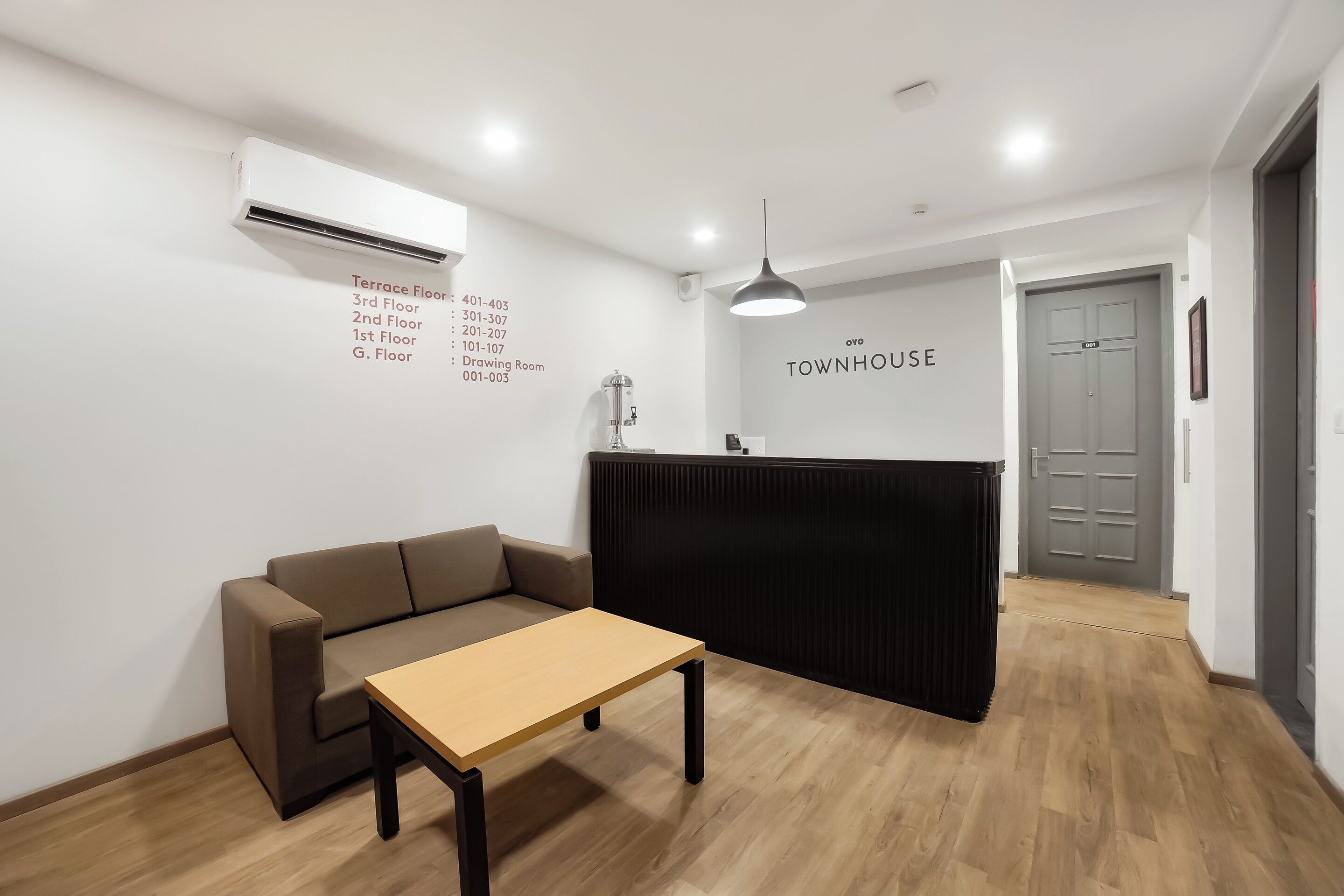 Una recepción con un cartel que dice 'TOWNHOUSE' y una lista de números de habitación en la pared.