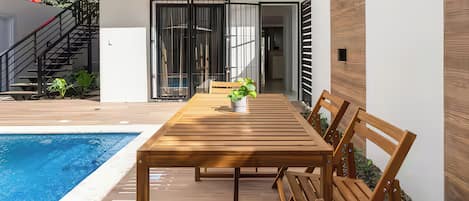 A modern outdoor patio with a pool, wooden furniture, and a view of the building's interior.