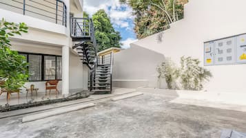 Un edificio moderno con un patio de concreto, una escalera en espiral y una pequeña zona de estar con sillas y una mesa.