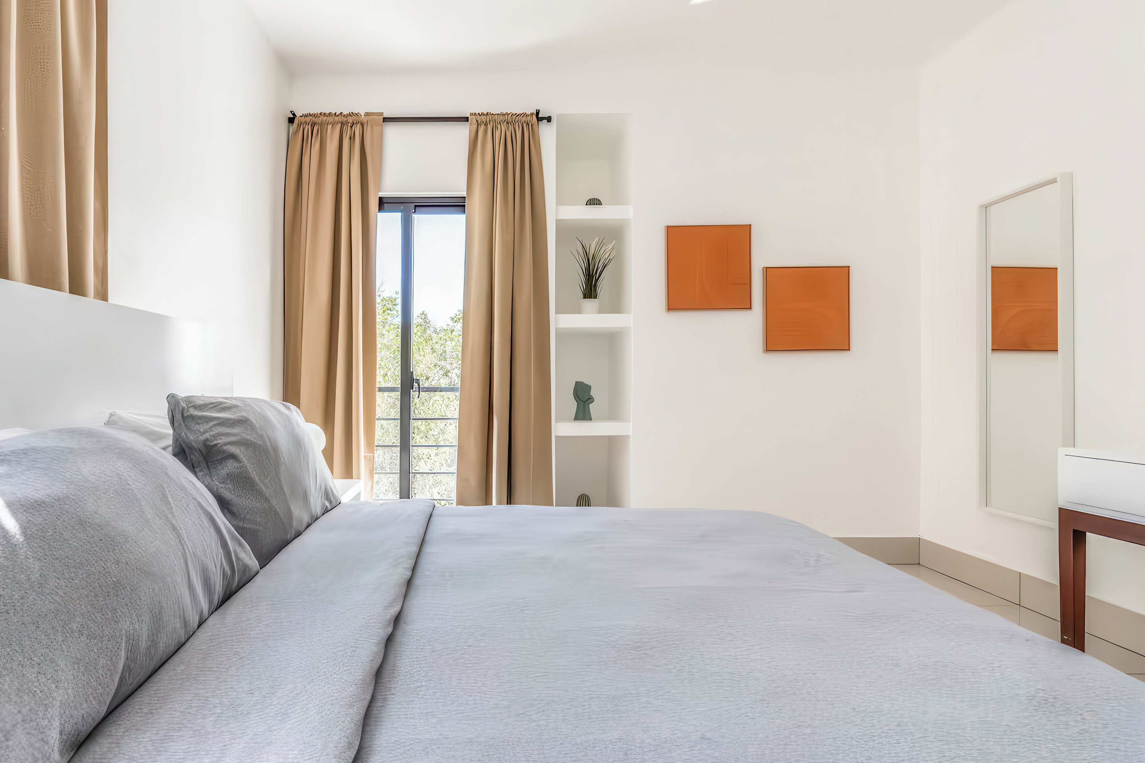 Un dormitorio moderno con cama, cortinas, una ventana y una pared con estanterías y obras de arte.