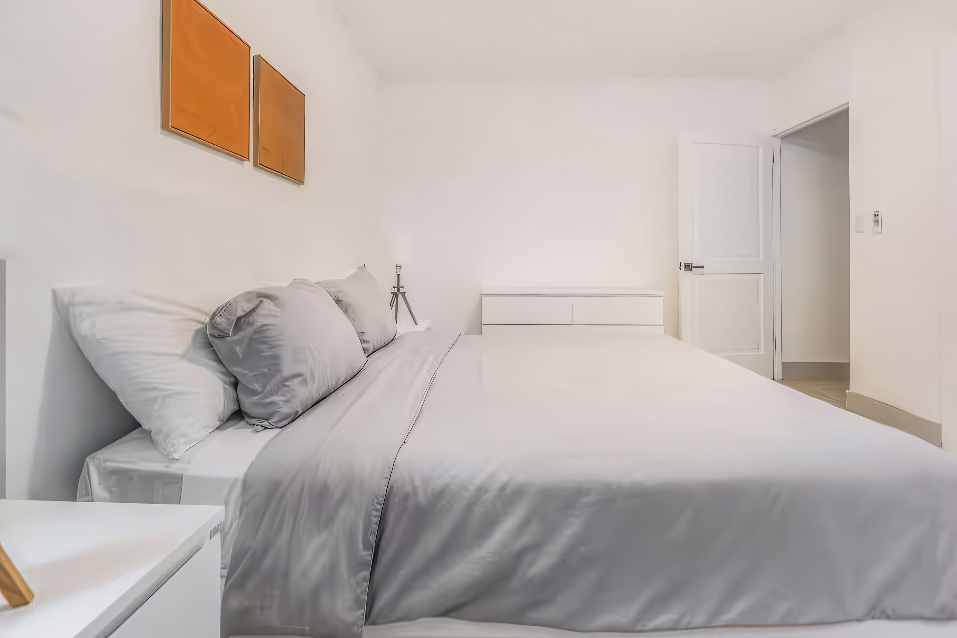 A minimalist bedroom with a bed, bedside table, and a door leading to another room.