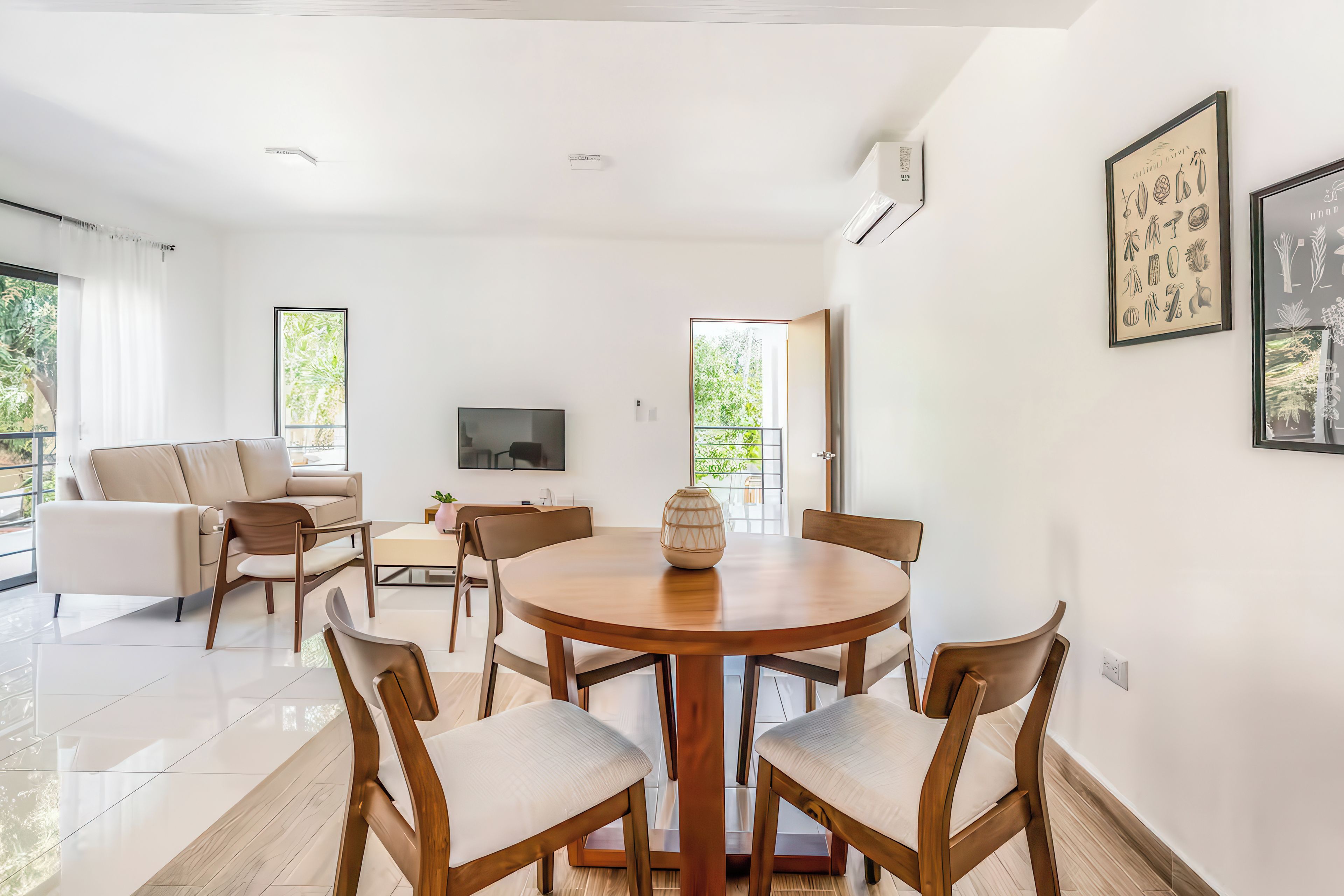 Un salon moderne avec une table ronde en bois, des canapés beiges et un téléviseur à écran plat.