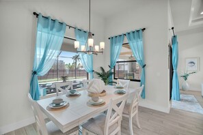 Ein Essbereich mit einem weißen Tisch, gedeckten Plätzen für vier Personen, blauen Vorhängen und einer Chandelier.